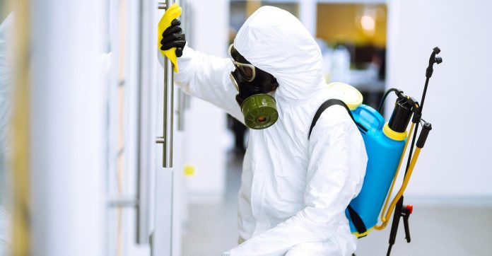 person wearing hazmat suit disinfecting a door